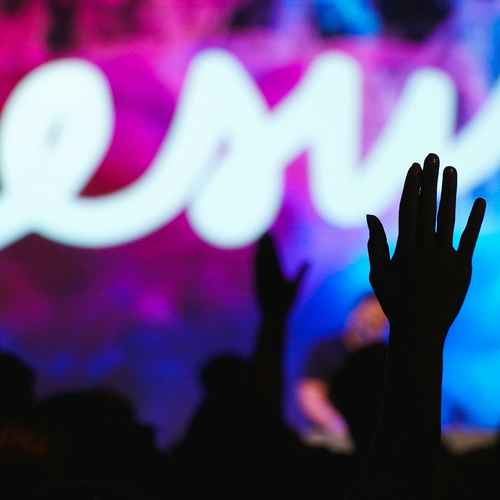 Viele Menschen mit erhobenen Menschen. Im Hintergrund ist auf einer Bühne das Wort Jesus zu lesen.